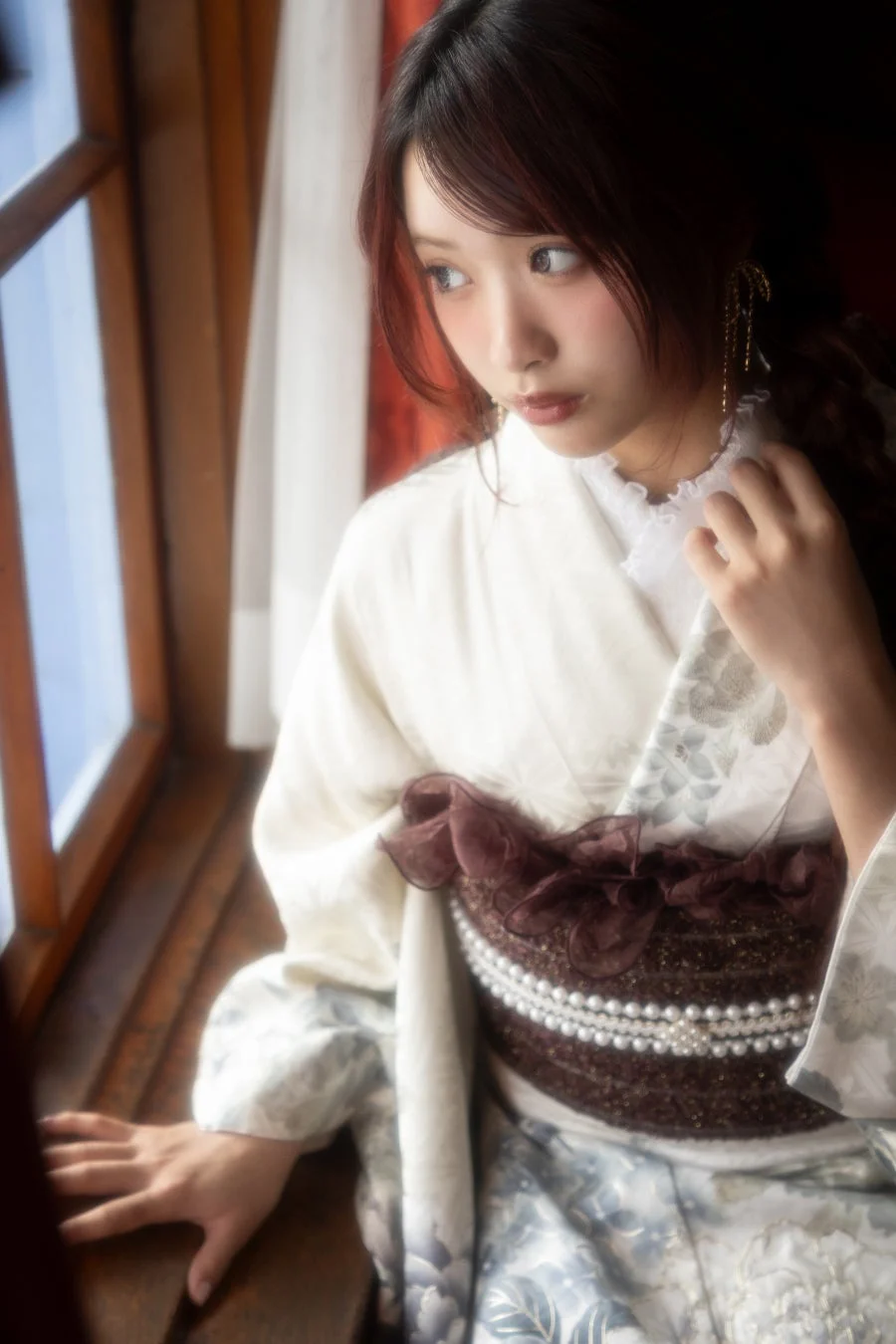 窓辺に座り物憂げな表情を見せる振袖姿の女性