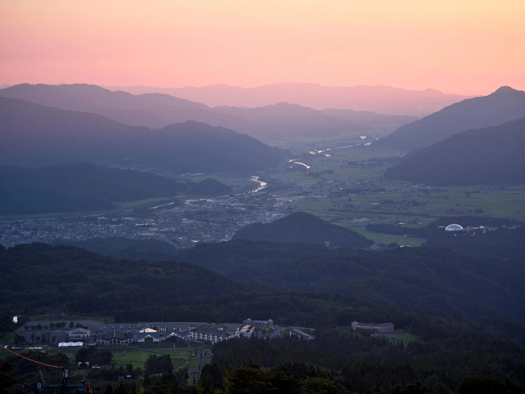 夕焼けに染まるピンク色の空の下、幾重にも連なる山々の広大な風景。